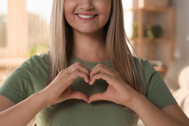 Photo of Happy volunteer making heart with her hands in room, closeup