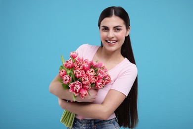 Happy young woman with beautiful bouquet on light blue background