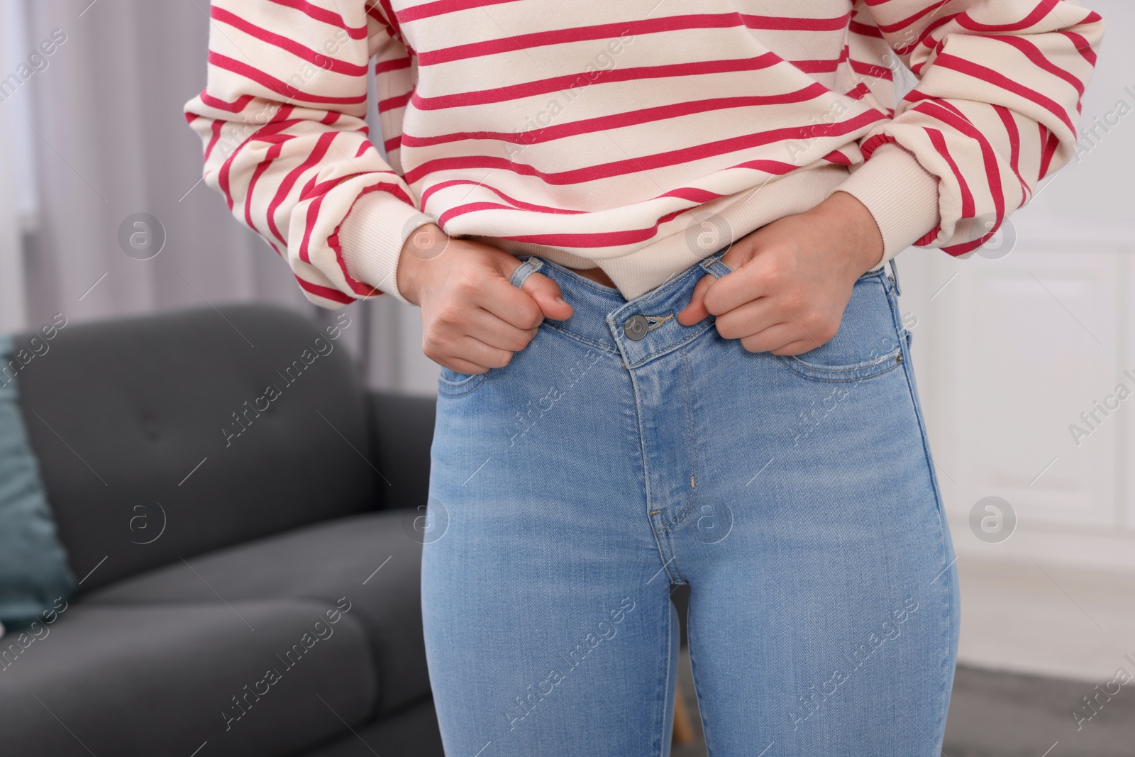 Photo of Woman trying to fit into her jeans at home, closeup