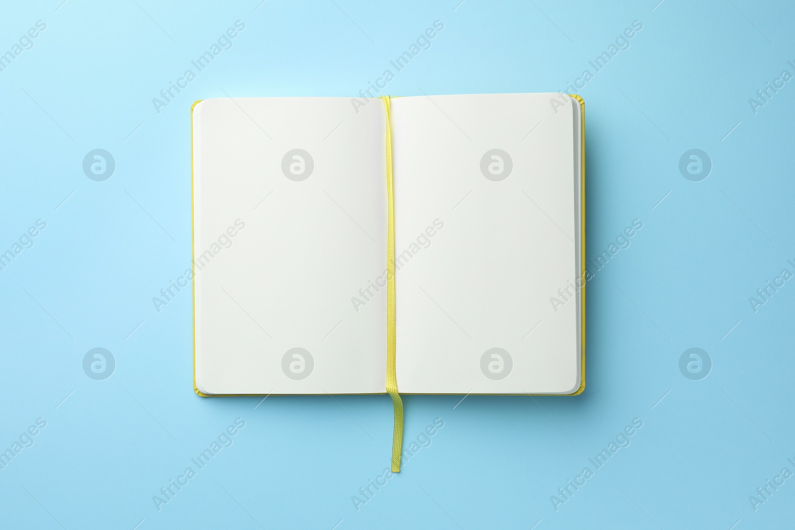 Photo of Open notebook with blank pages on light blue background, top view. Space for text