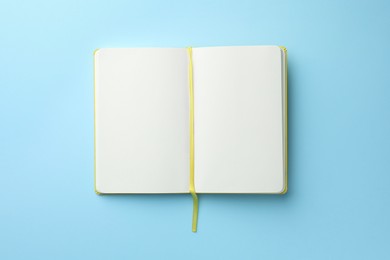 Photo of Open notebook with blank pages on light blue background, top view. Space for text