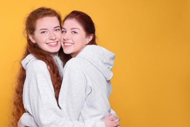 Photo of Portrait of beautiful young redhead sisters on orange background. Space for text