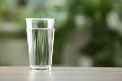 Photo of Glass of water on white table against blurred green background, closeup. Space for text