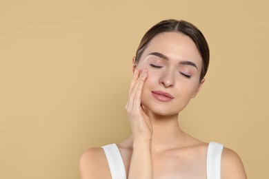 Young woman applying cream under eyes on beige background, space for text