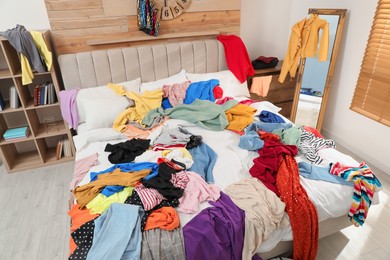 Photo of Pile of clothes on bed in messy room. Fast fashion concept