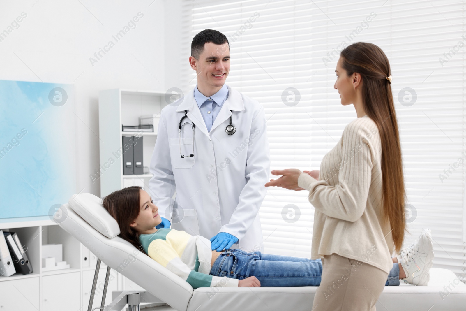 Photo of Gastroenterologist examining girl with stomach ache on couch in clinic