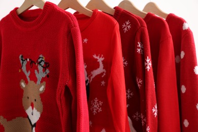 Photo of Different Christmas sweaters hanging on rack against white background, closeup