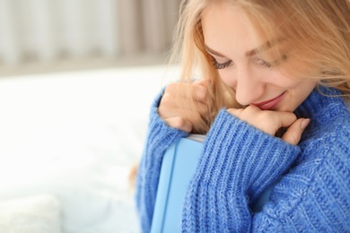 Beautiful young woman sitting with book on bed and dreaming at home. Winter atmosphere