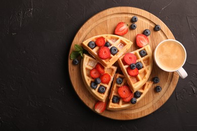 Tasty Belgian waffles with fresh berries and cup of coffee on black table, top view. Space for text