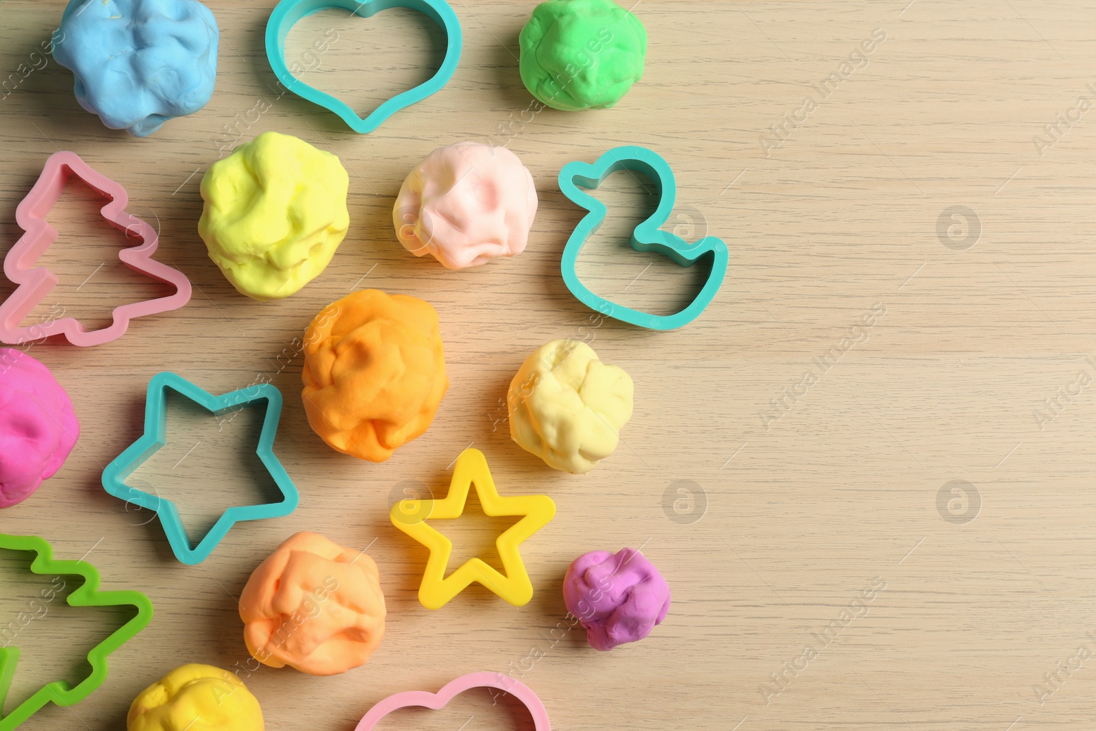 Photo of Different color play dough with molds on wooden table, flat lay. Space for text
