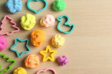 Different color play dough with molds on wooden table, flat lay. Space for text