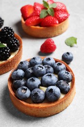 Photo of Tartlets with different fresh berries on light table. Delicious dessert