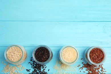 Jars with different types of rice on blue wooden background, top view. Space for text