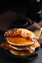 Photo of Delicious pancakes with maple syrup and fried bacon on black table