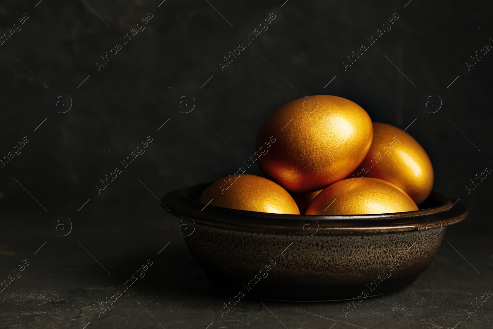 Photo of Bowl with golden eggs on black table, space for text