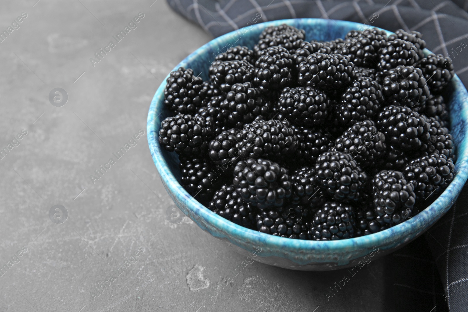 Photo of Bowl of ripe blackberries on grey table, space for text