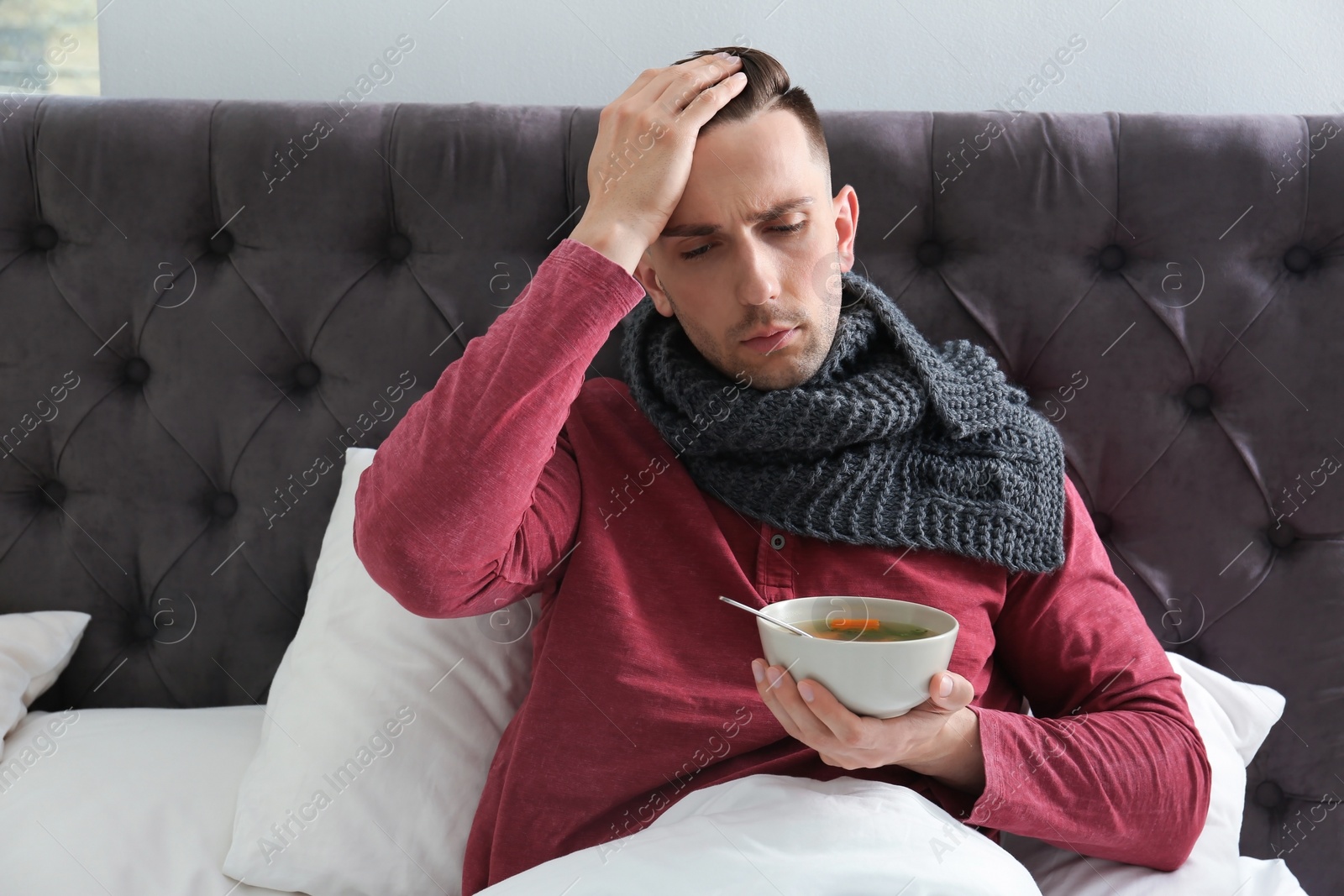 Photo of Sick young man eating broth to cure cold in bed at home