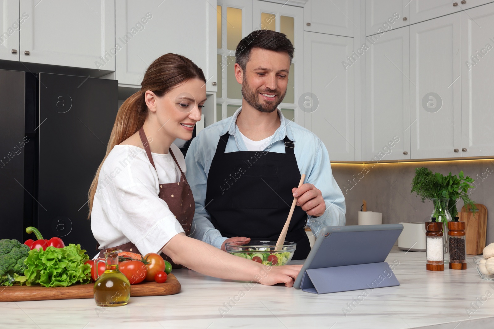 Photo of Happy couple reading recipe on tablet while cooking in kitchen. Online culinary book