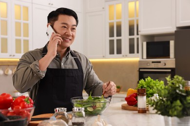 Photo of Man talking on smartphone while cooking in kitchen