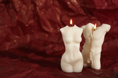 Photo of Beautiful burning male and female body shaped candles on red crumpled parchment. Space for text