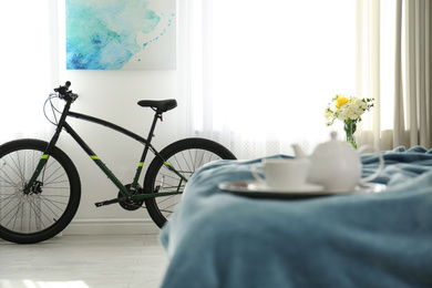 Photo of Stylish room interior with tea set on bed and modern bicycle