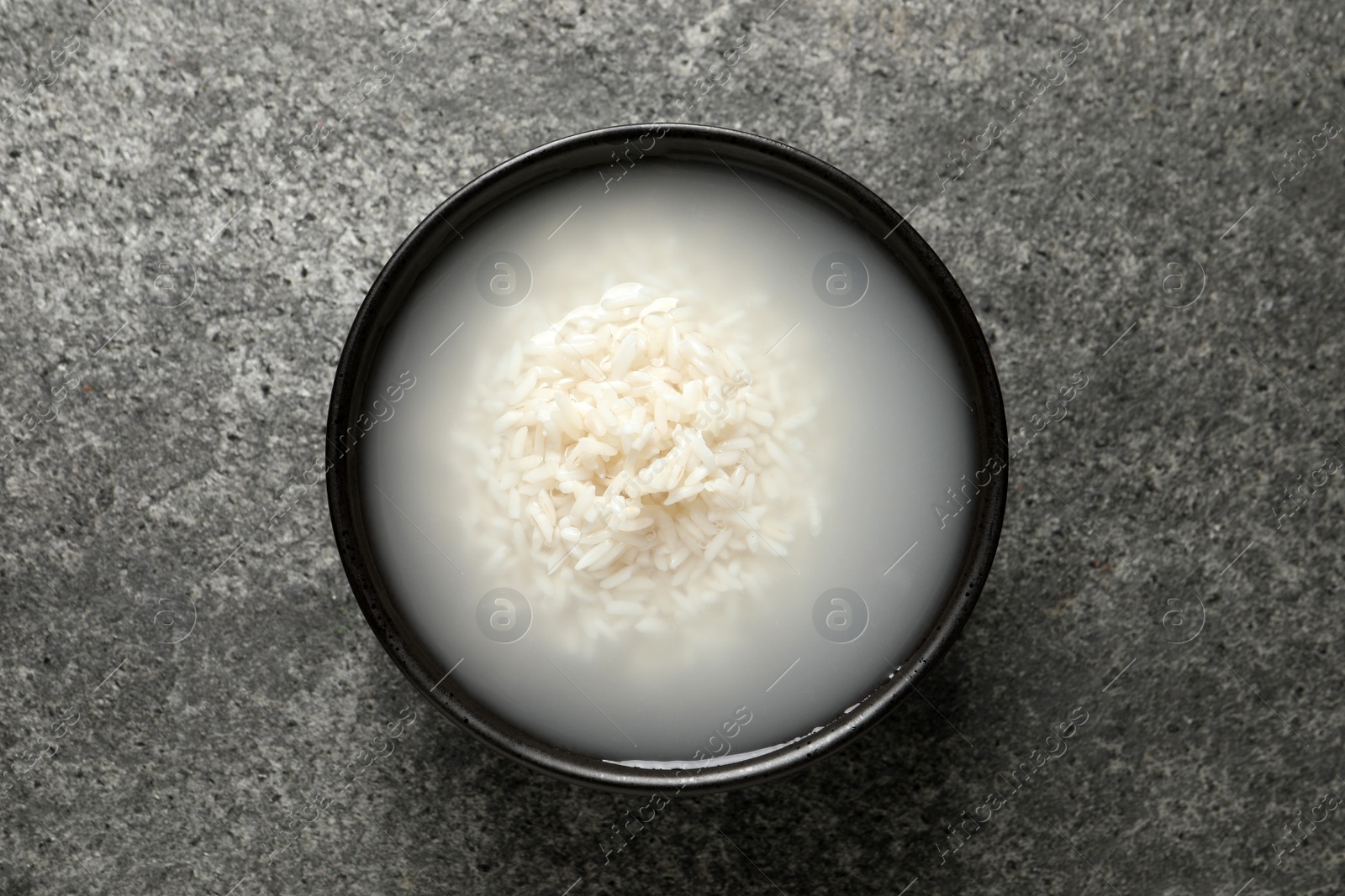 Photo of Bowl with rice soaked in water on grey table, top view