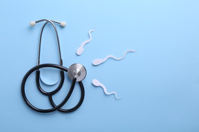 Photo of Reproductive medicine. Figures of sperm cells and stethoscope on light blue background, flat lay with space for text