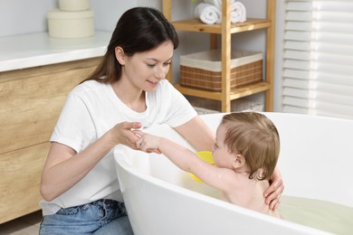 Mother bathing her cute little baby in tub at home