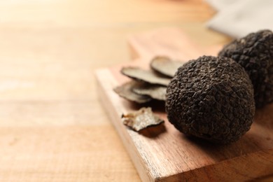 Photo of Black truffles with board on wooden table, closeup. space for text