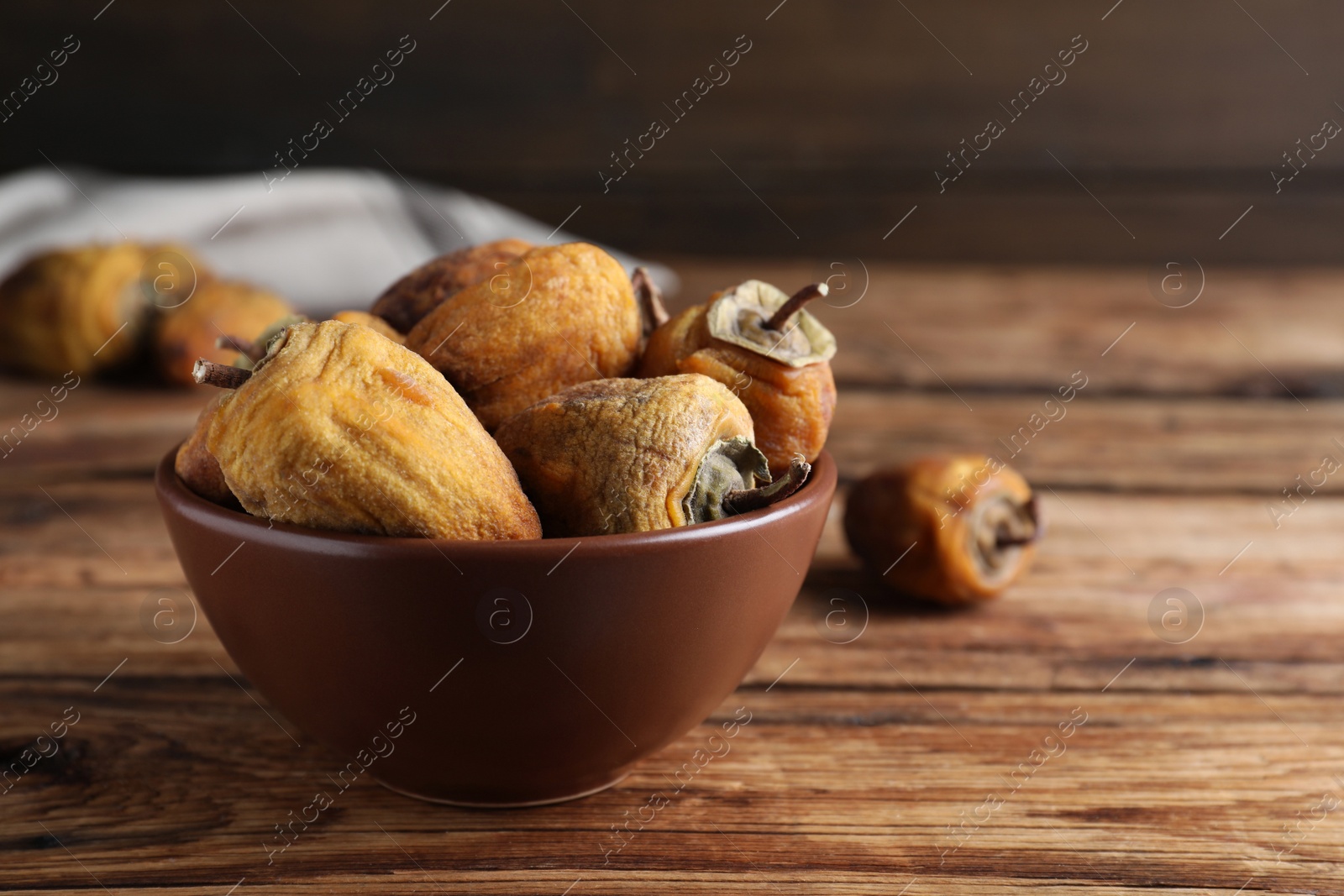 Photo of Bowl with tasty dried persimmon fruits on wooden table, space for text