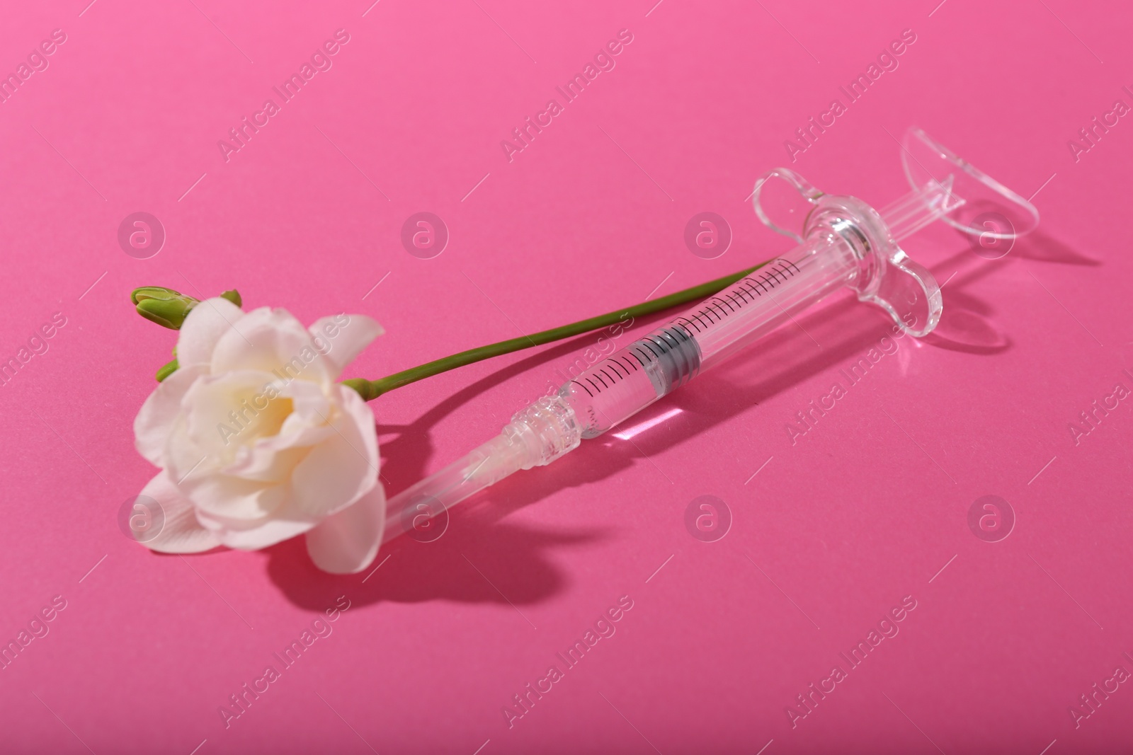 Photo of Cosmetology. Medical syringe and freesia flower on pink background