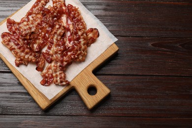 Photo of Slices of tasty fried bacon on wooden table, top view. Space for text