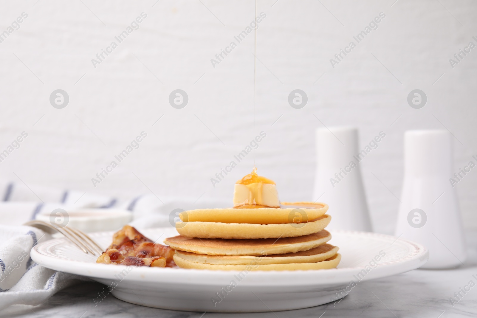 Photo of Delicious pancakes with butter, maple syrup and fried bacon on white marble table