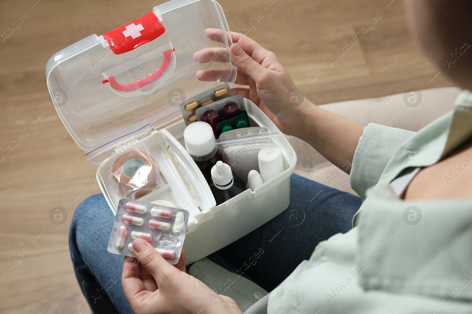 Photo of Woman putting pills into first aid kit indoors, closeup