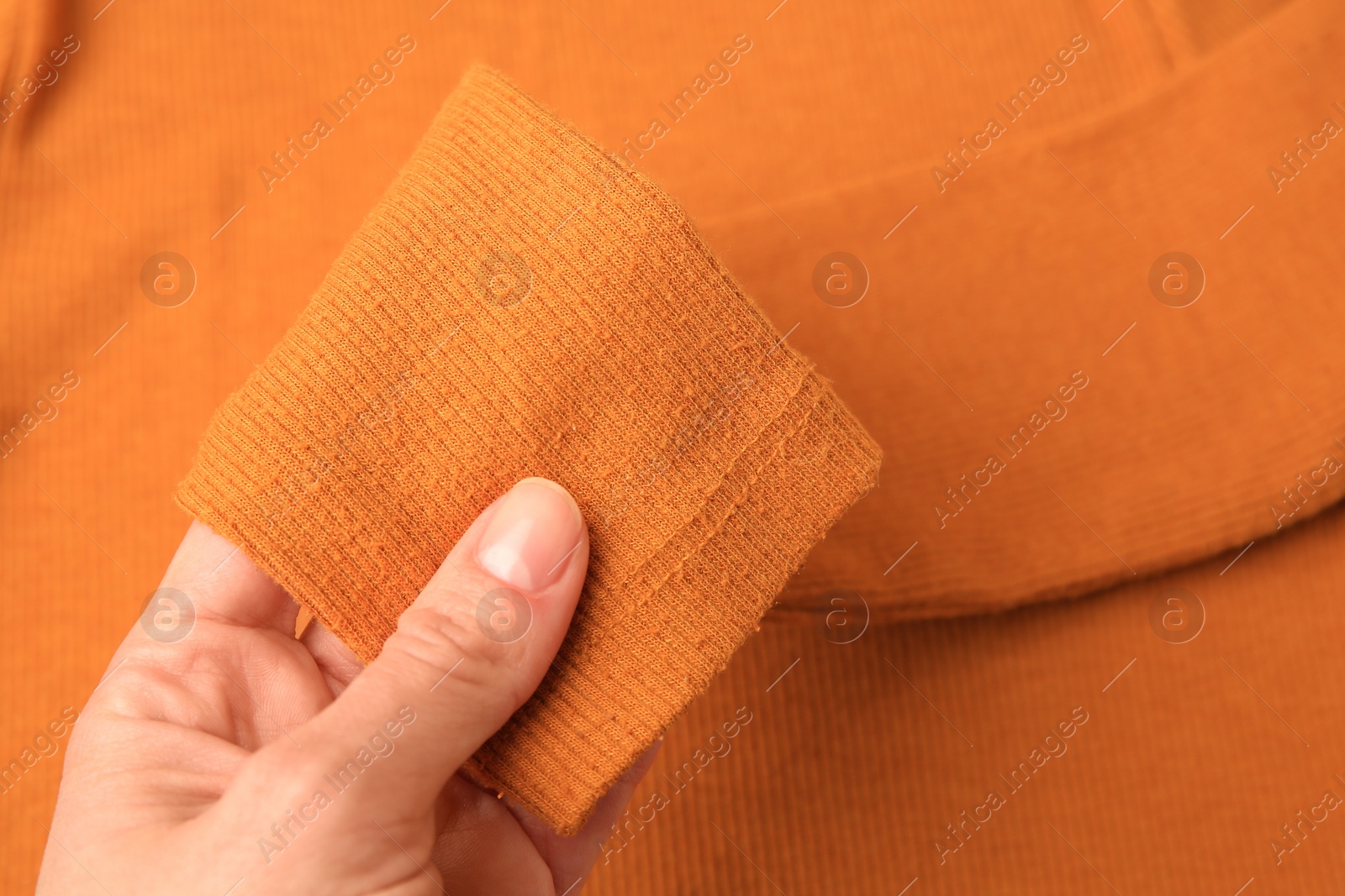 Photo of Woman holding sleeve of orange sweater with lint as background, top view. Before using fabric shaver