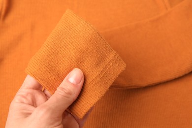 Photo of Woman holding sleeve of orange sweater with lint as background, top view. Before using fabric shaver