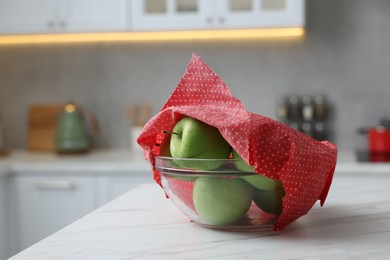 Apples in bowl covered with beeswax food wrap on white table space for text