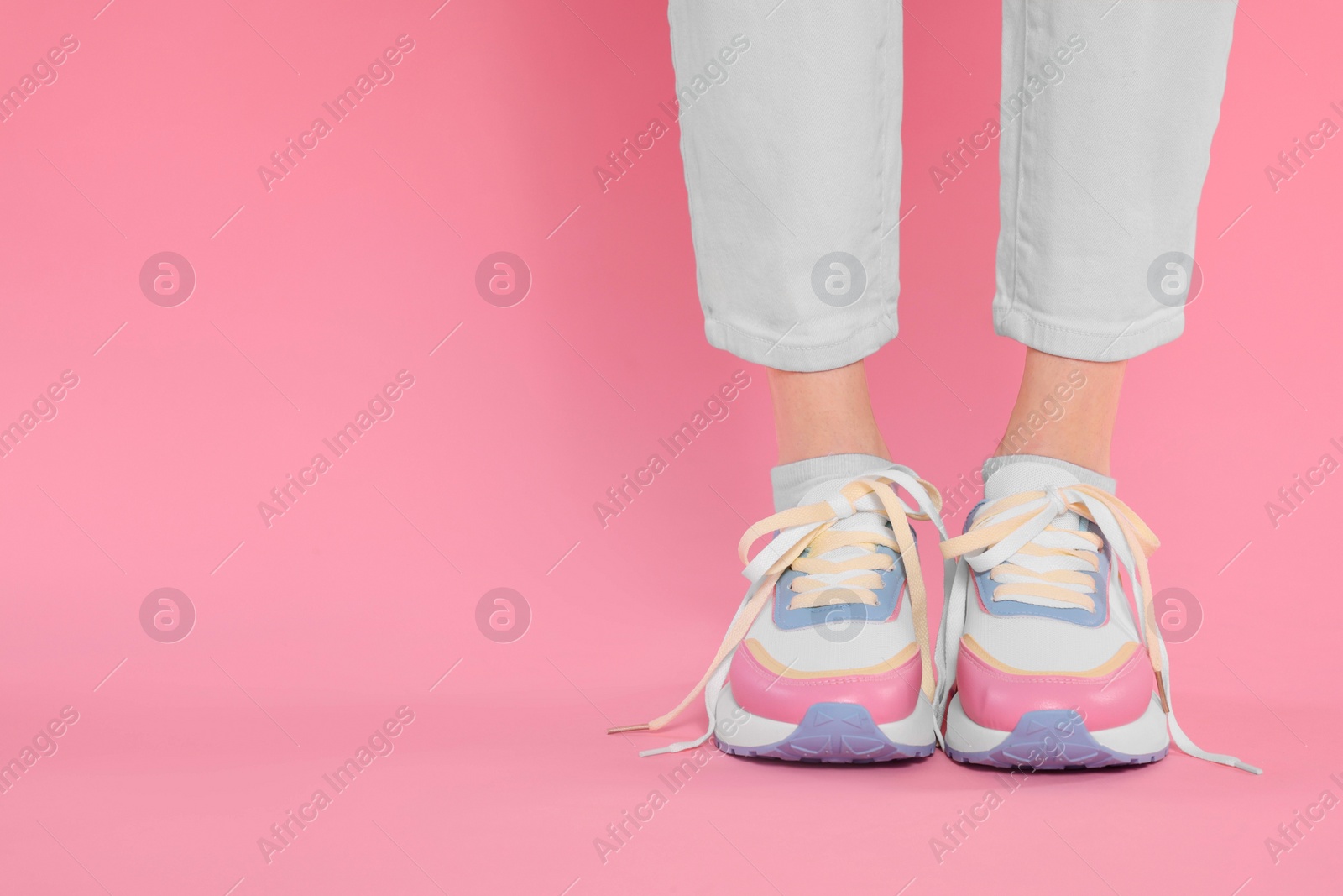 Photo of Woman wearing new stylish sneakers on pink background, closeup. Space for text