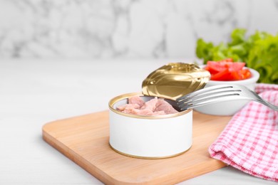 Photo of Tin can with canned tuna and fork on white table