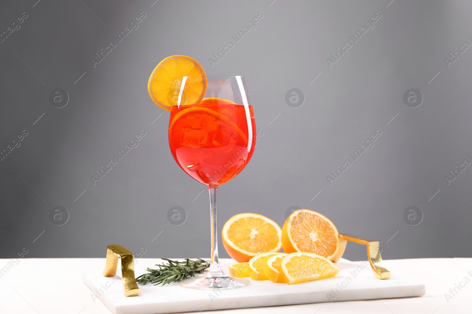 Photo of Glass of tasty Aperol spritz cocktail with orange slices and rosemary on white table against gray background