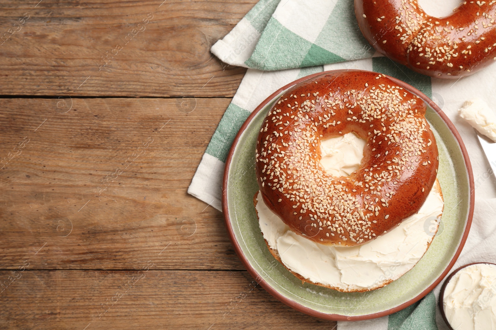 Photo of Delicious bagel with cream cheese on wooden table, flat lay. Space for text