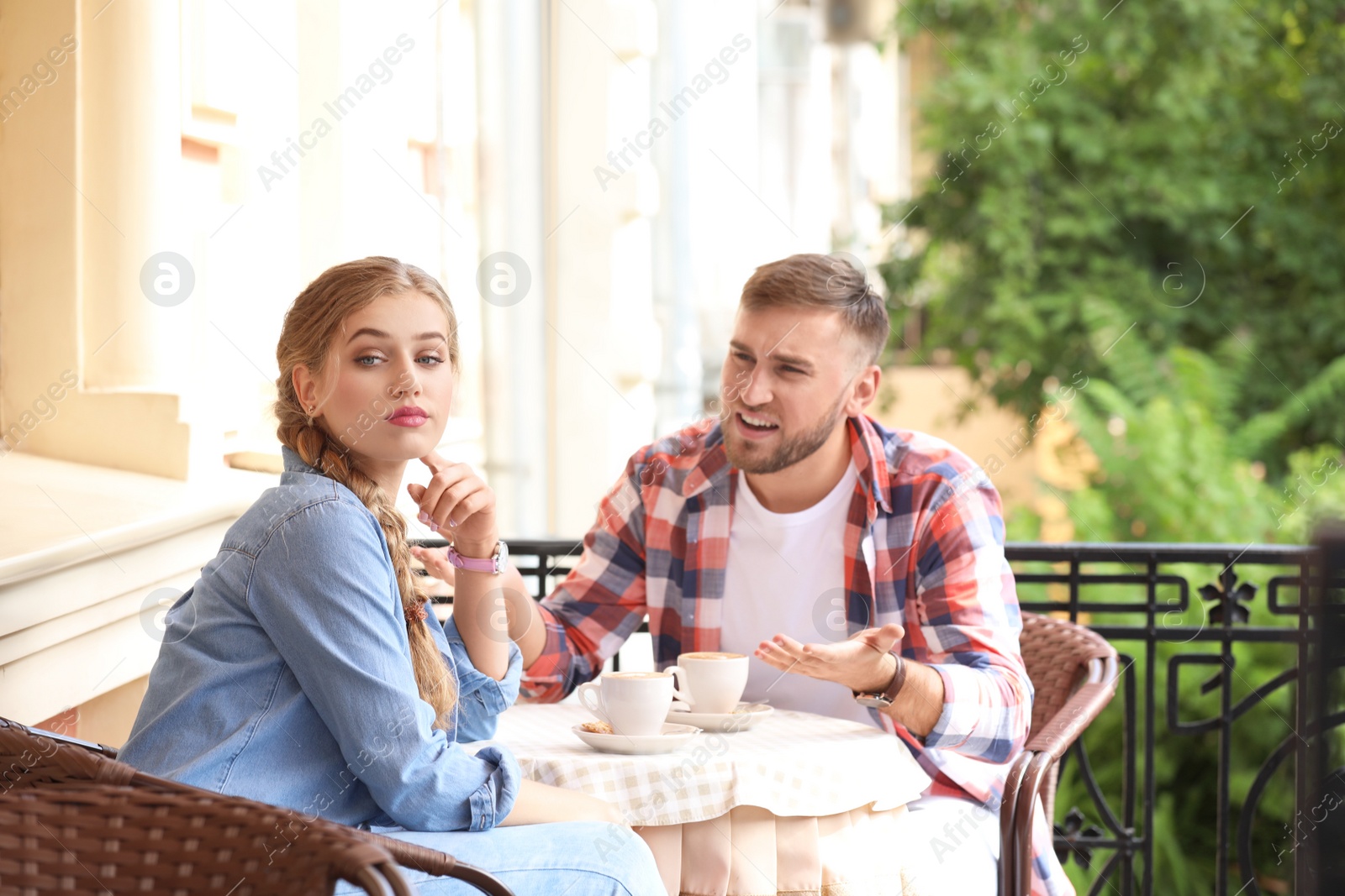 Photo of Young couple arguing while sitting in cafe, outdoors. Problems in relationship