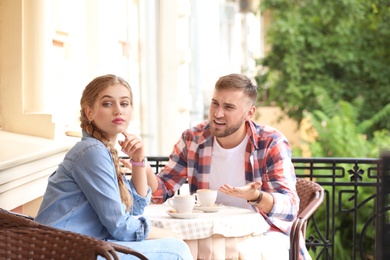 Photo of Young couple arguing while sitting in cafe, outdoors. Problems in relationship