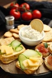 Different snacks with salted crackers on wooden board, closeup
