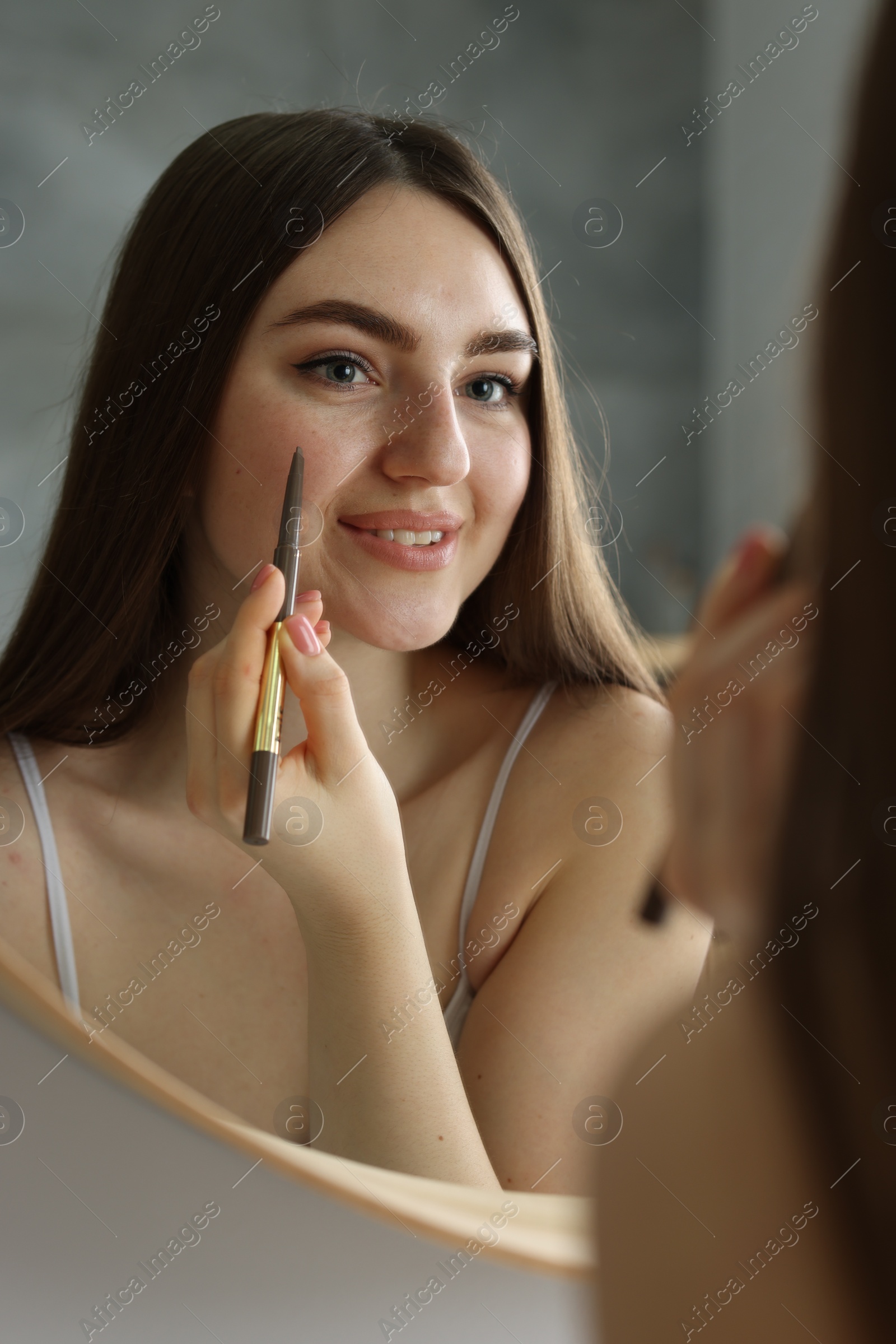 Photo of Smiling woman drawing freckles with pen near mirror indoors