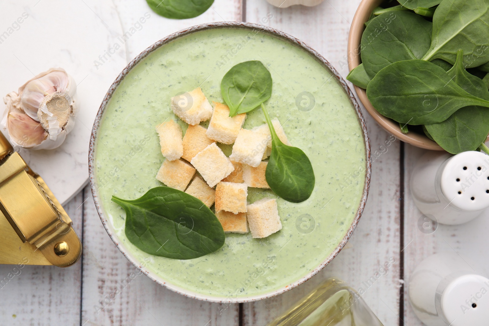 Photo of Delicious spinach cream soup with leaves and croutons in bowl on white wooden table, flat lay