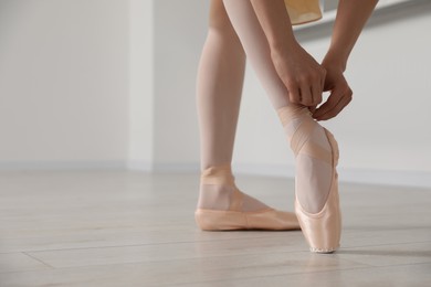 Ballerina tying pointe shoes in dance studio, closeup. Space for text