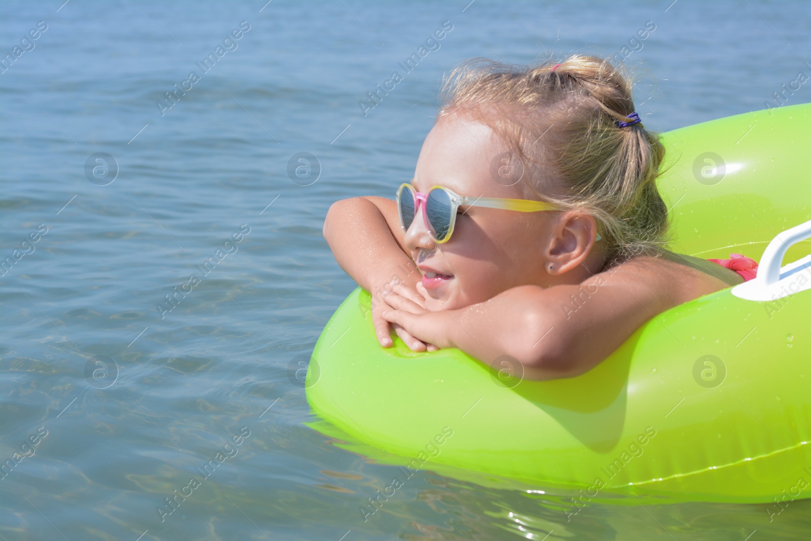Photo of Little girl with inflatable ring in sea on sunny day, space for text
