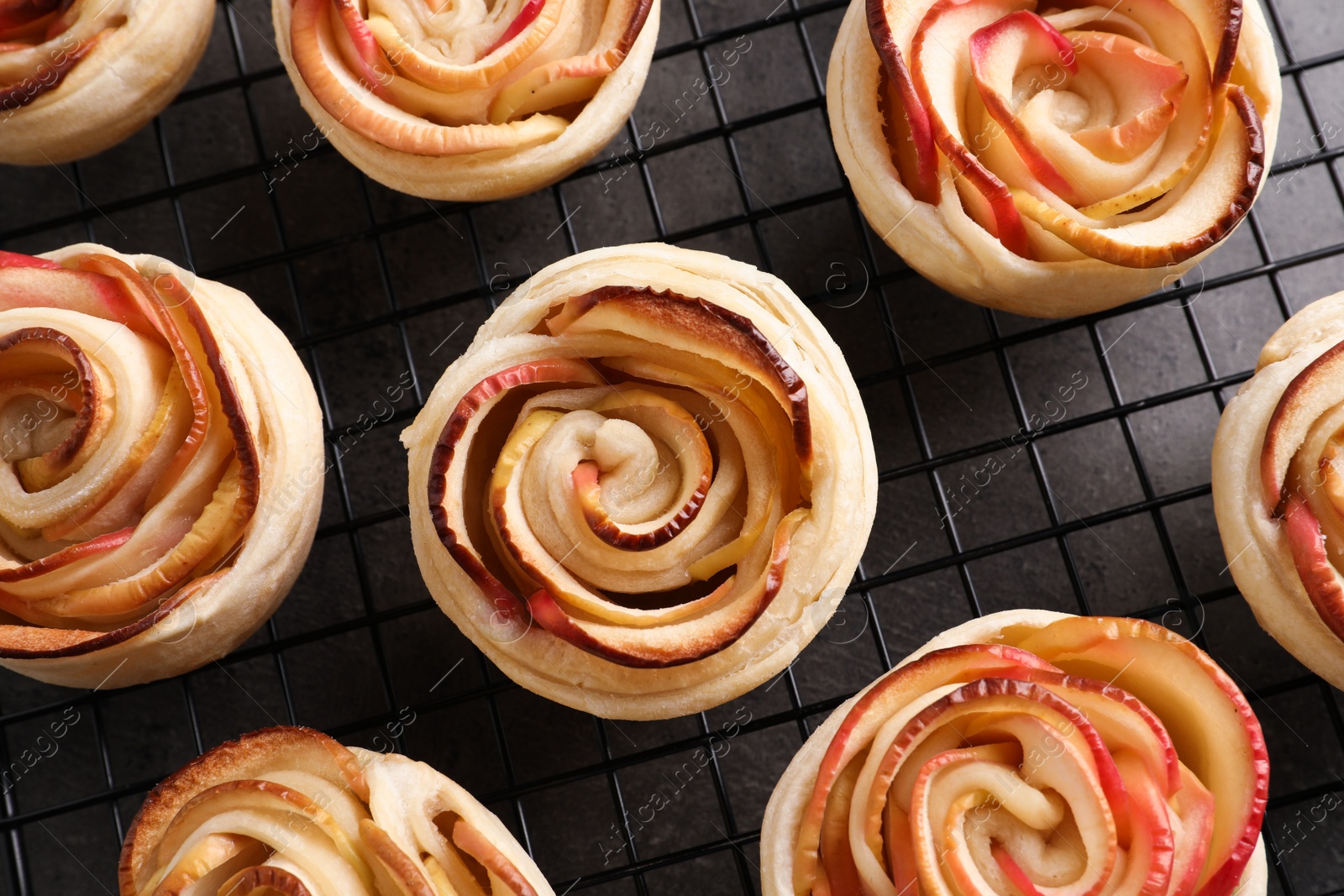 Photo of Cooling rack with freshly baked apple roses pastry on grey table, flat lay. Beautiful dessert