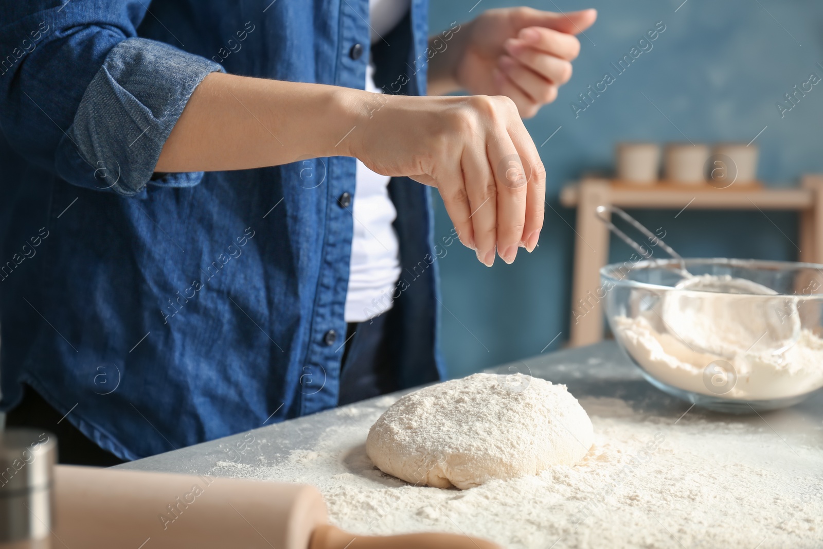 Photo of Woman sprinkling flour over dough on table in kitchen